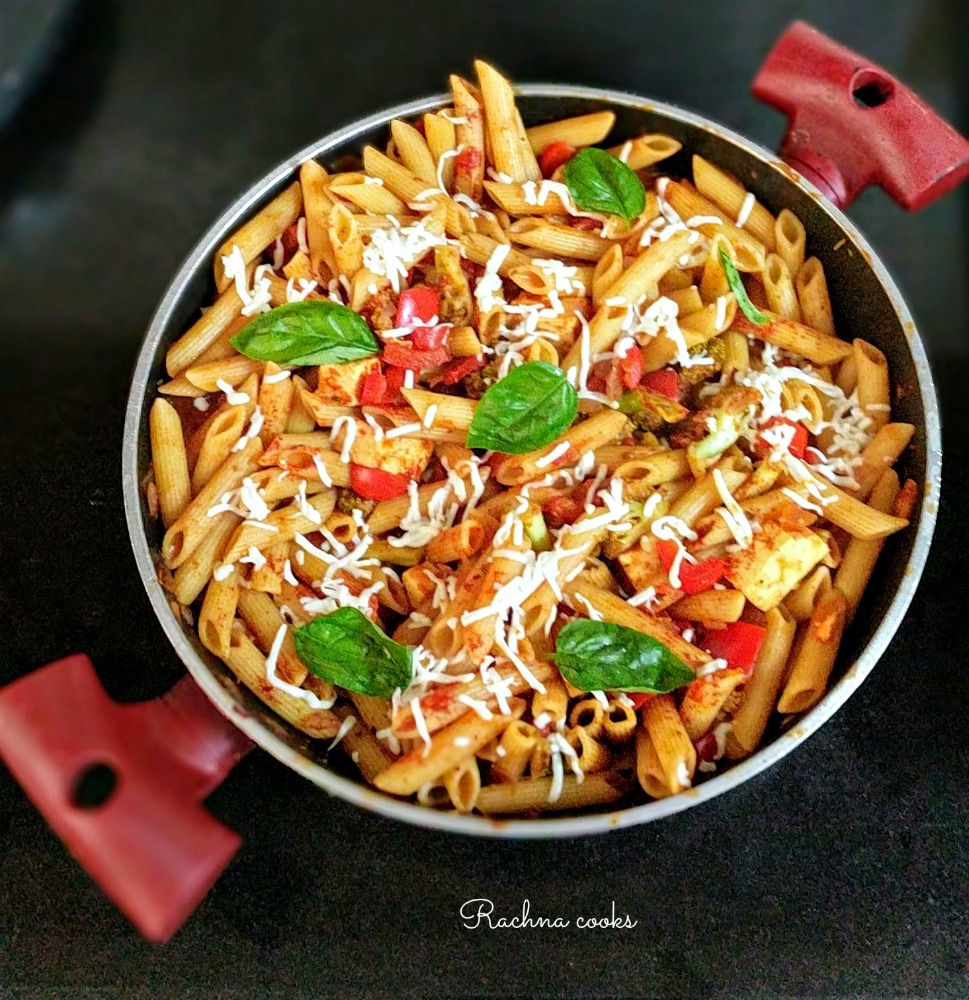 Pasta in tomato sauce in a wok with basil leaves on top.