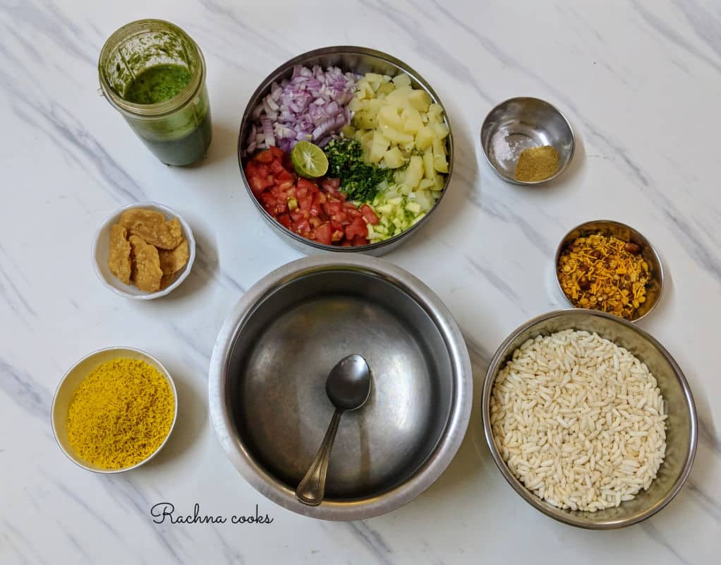 Ingredients to prepare bhel puri on a frame: murmura, sev, chutney, chopped veggies, mixture, papdi, spices.
