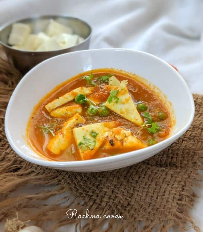 Paneer and peas curry in a white bowl with a brown mat background.